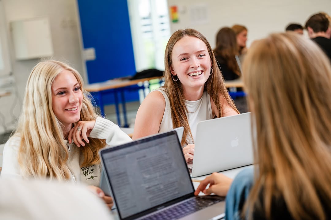 HHX-elever griner og samarbejder om en opgave på deres bærbare computer
